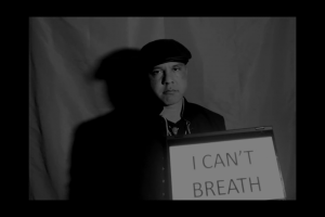 Black and white image of Alan holding a screen that reads "I can't breath"